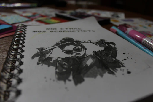 A close-up of hands sketching vibrant ideas in a notebook, surrounded by scattered art supplies.