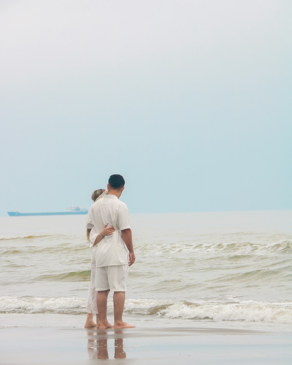 a man and a woman standing on a beach next to the ocean