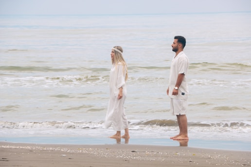 a man and a woman standing on a beach next to the ocean