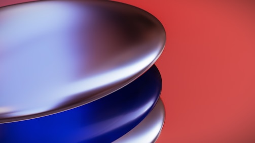 Metallic, curved surfaces are layered against a vibrant red background, creating a sleek and modern aesthetic. The shiny, reflective material reflects light, giving the surfaces a smooth and glossy appearance.