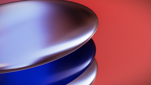 Metallic, curved surfaces are layered against a vibrant red background, creating a sleek and modern aesthetic. The shiny, reflective material reflects light, giving the surfaces a smooth and glossy appearance.