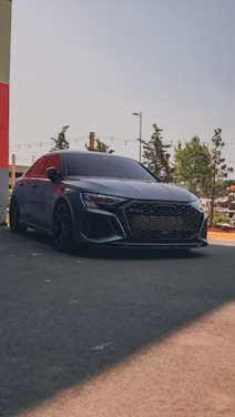 A sleek red and black rental car parked in front of a modern city backdrop under clear skies.