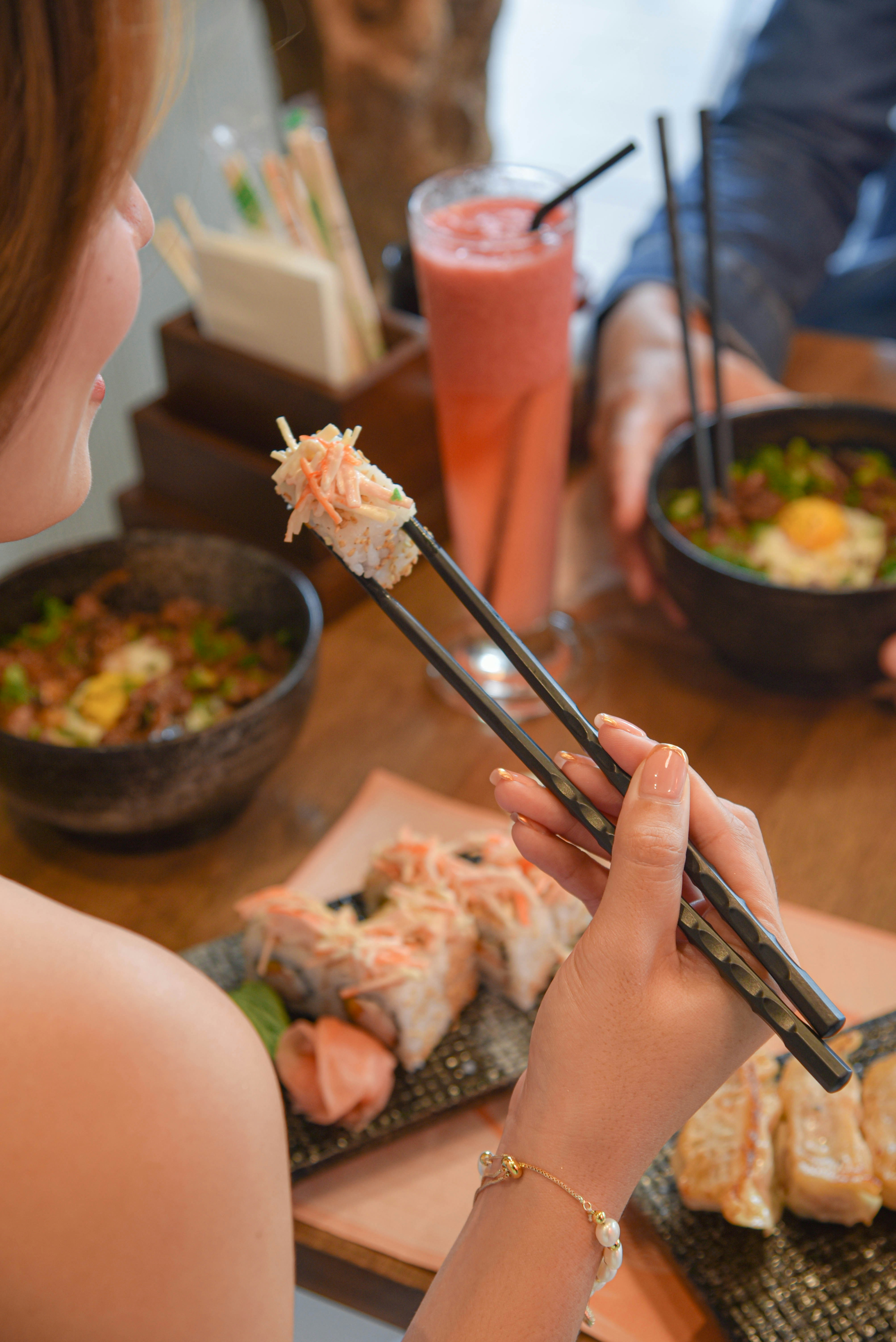 Une femme mangeant des sushis avec des baguettes à une table