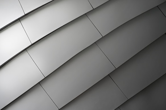 A series of metallic panels arranged in an overlapping, diagonal pattern, creating a sleek, modern texture. The surface reflects light subtly, emphasizing the smoothness and uniformity of the material.