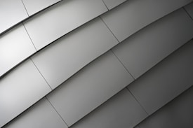 A series of metallic panels arranged in an overlapping, diagonal pattern, creating a sleek, modern texture. The surface reflects light subtly, emphasizing the smoothness and uniformity of the material.