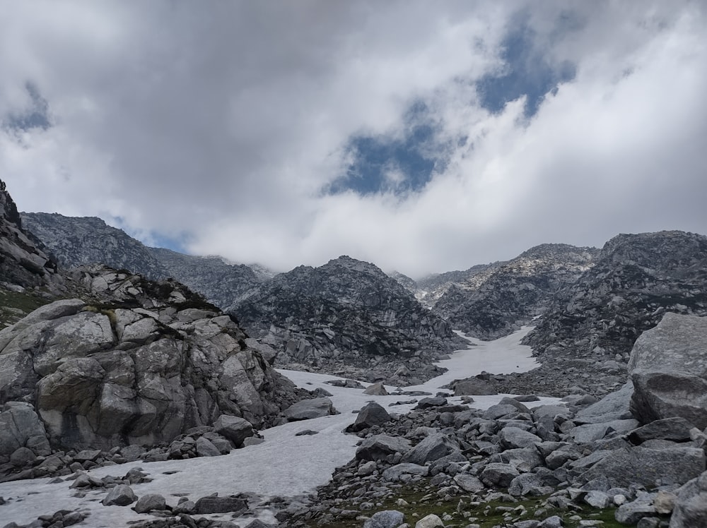 a rocky area with snow on the ground and mountains in the background