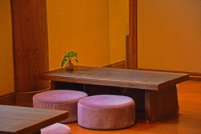 Minimalist interior corner with a warm cream wall, green plants, and a wooden table set for tea.