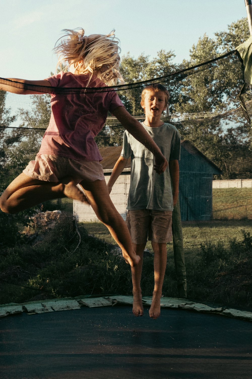 a young girl jumping on a trampoline while a man watches