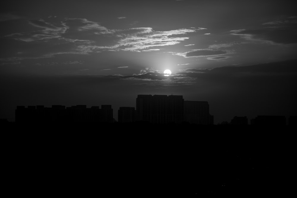 a black and white photo of the sun setting over a city