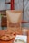 A neatly arranged snack setup featuring a large brown paper bag filled with sugared pastries, placed on a wooden table. In front of the bag, small golden brown bites are scattered, with some in a wicker basket. Nearby, there is a glass filled with iced coffee or tea, and an open book with a pair of reading glasses resting on it, providing a cozy and inviting atmosphere.