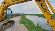 Heavy machinery carefully shaping a wetland area under a bright blue sky.