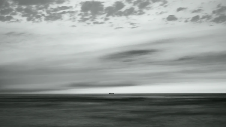 A vintage naval battleship cutting through stormy seas under a dramatic sky.