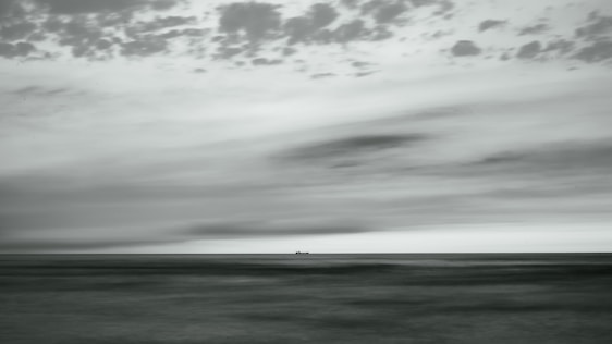 Black and white cinematic photo of a ship's bow cutting through vast ocean waves under a dramatic sky.