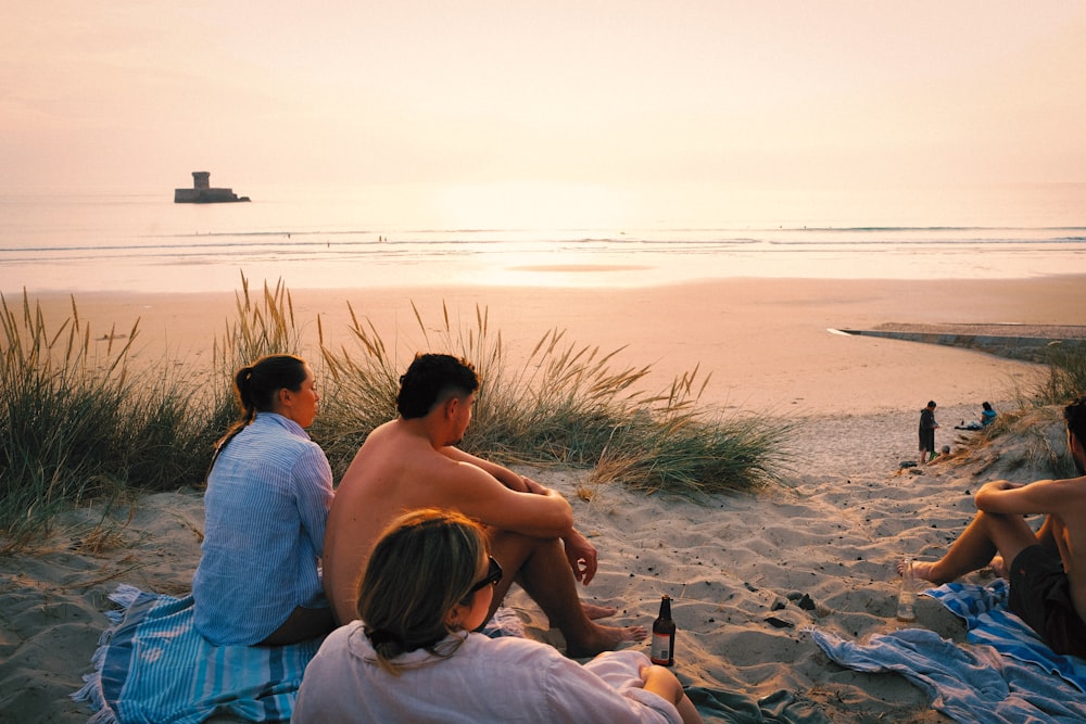 a group of people sitting on top of a sandy beach