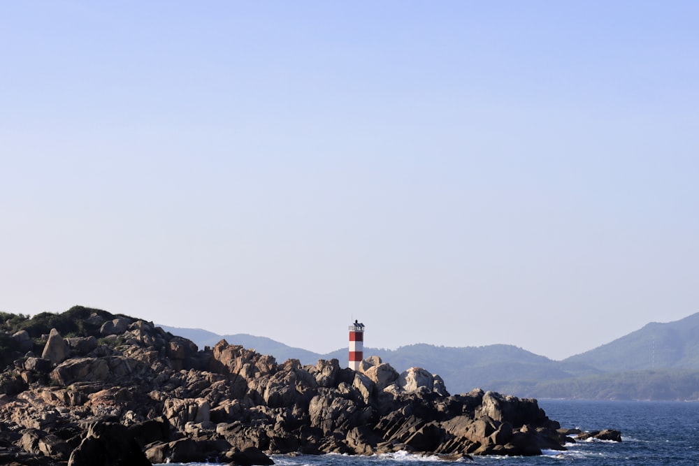 a red and white lighthouse sitting on top of a rocky shore