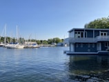 Modern floating house nestled among boats in a peaceful marina setting.