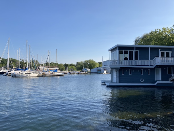 A peaceful waterfront view featuring a modern houseboat surrounded by calm water and greenery.