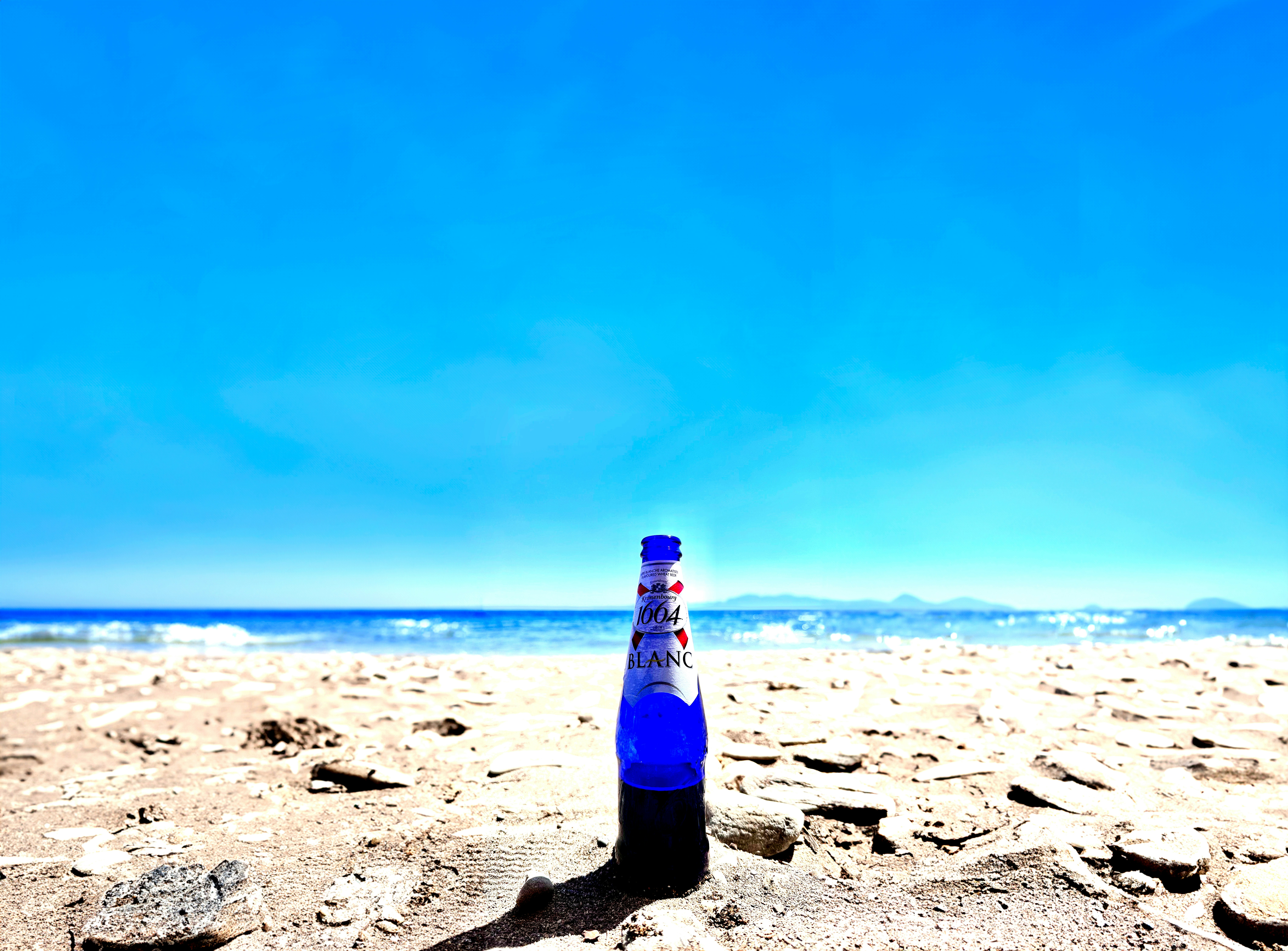 a bottle of beer sitting on top of a sandy beach