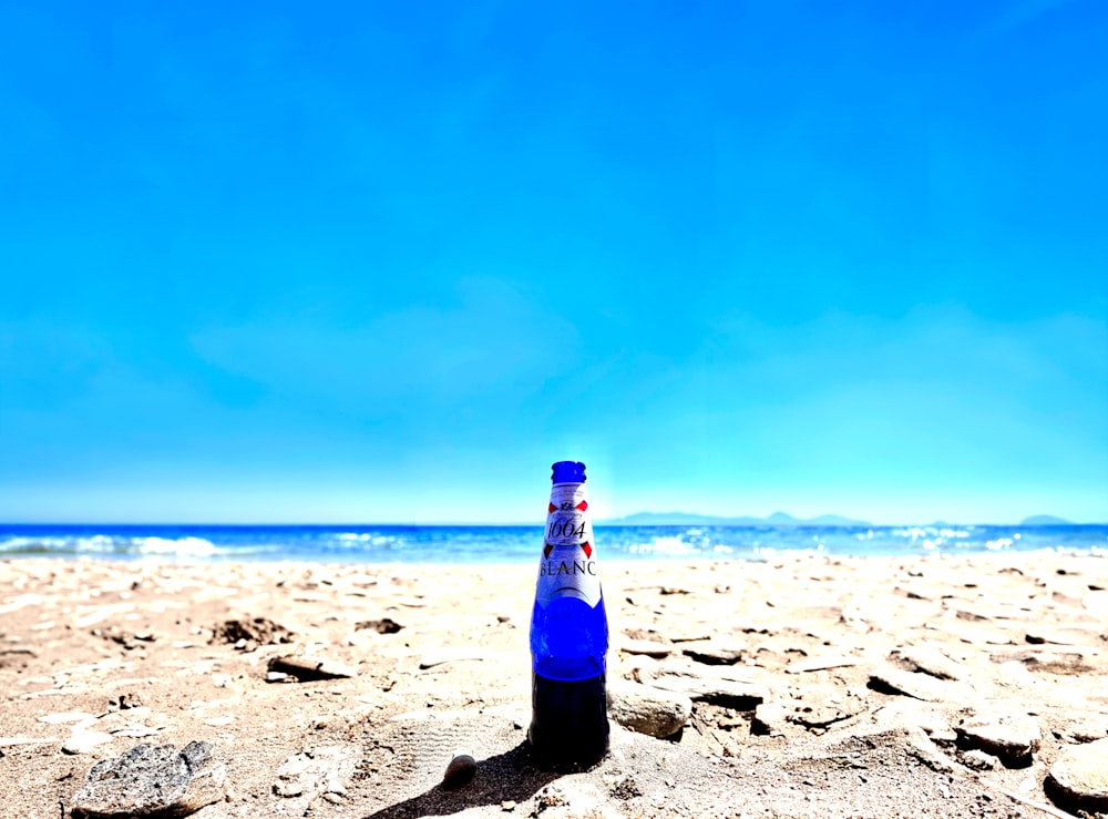 a bottle of beer sitting on top of a sandy beach