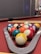 A neatly arranged set of pool balls sits within a triangular rack on a red felt pool table, accompanied by two cue sticks lying parallel to each other.