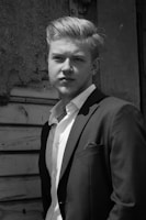 A polished portrait of Duncan Brand in a sharp suit against a soft grey background.