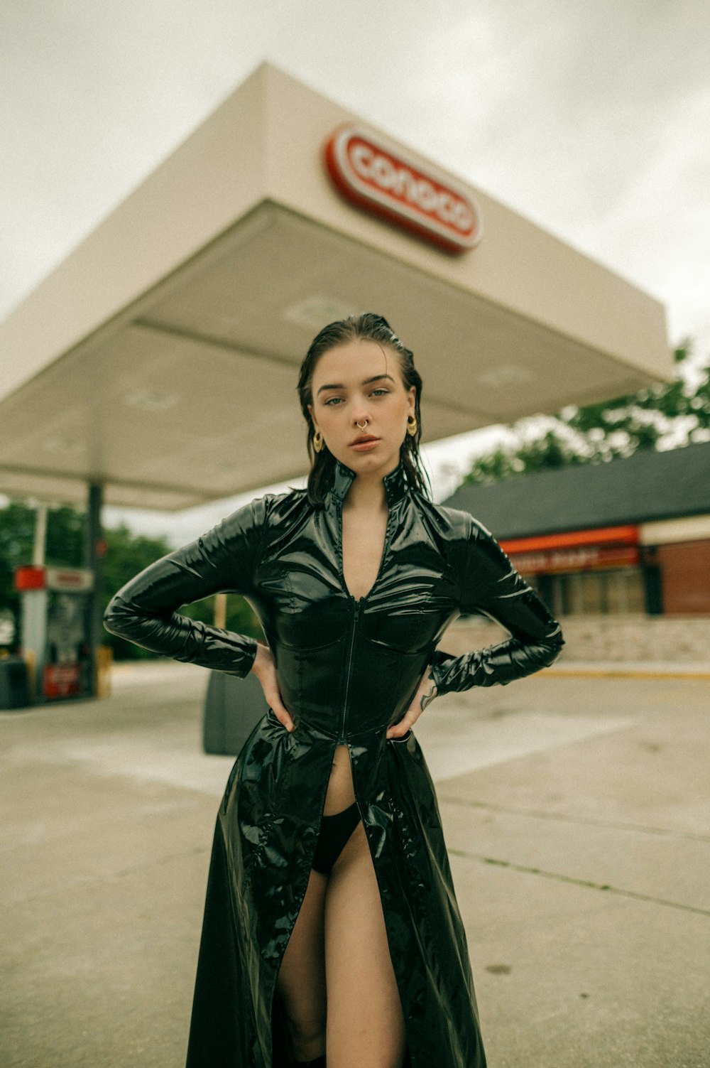 a woman in a leather outfit standing in front of a gas station