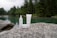 Skincare products are placed on a large rock near a serene lake surrounded by a dense forest. The water is clear, reflecting the green hues of the surrounding trees, creating a tranquil and natural setting.