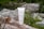 A cosmetic tube labeled 'Plantae Bio Crema Corpo' is placed on a log surrounded by natural vegetation and rocks, depicting an outdoor setting.