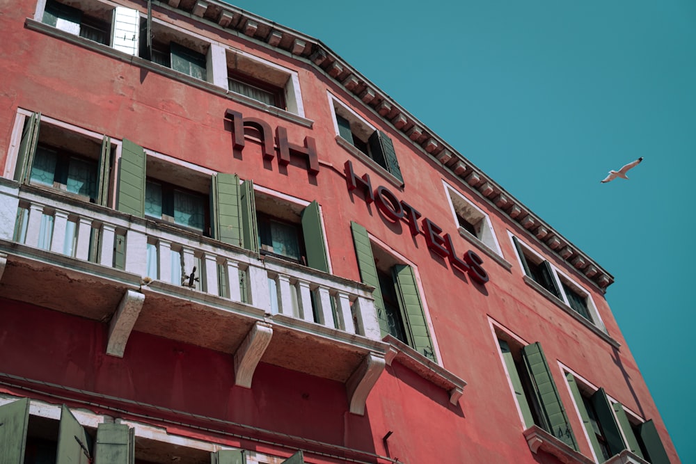 a red building with green shutters and a plane flying in the sky