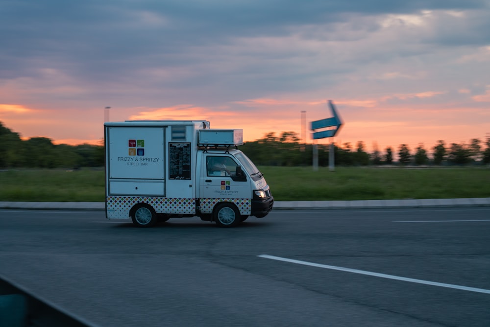 a white truck driving down a street next to a lush green field