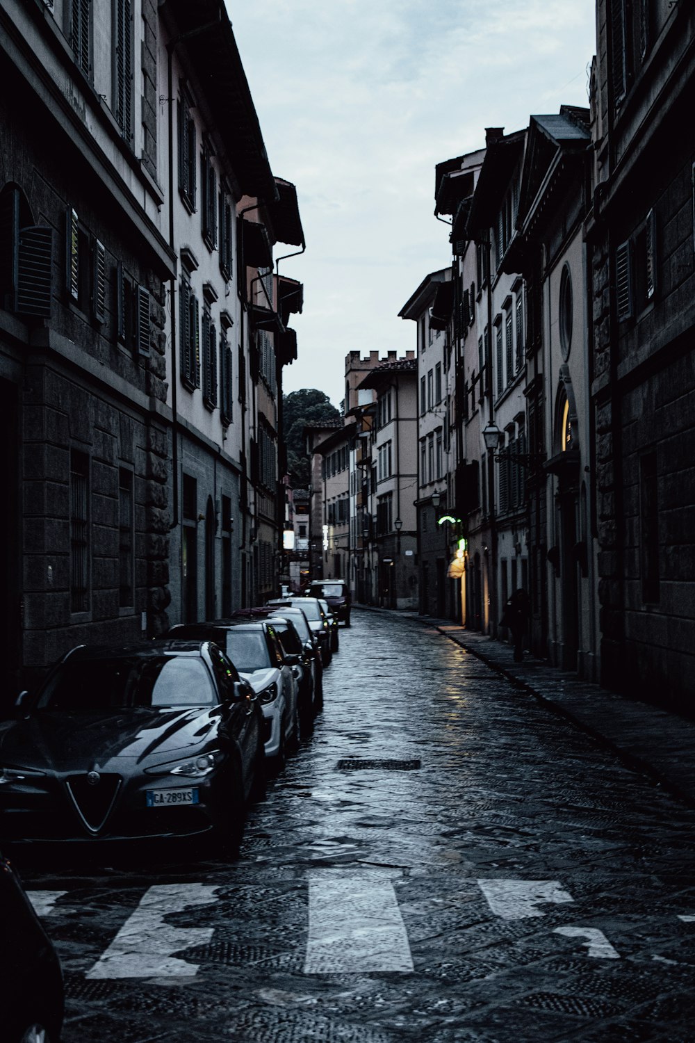 a city street lined with parked cars under a cloudy sky