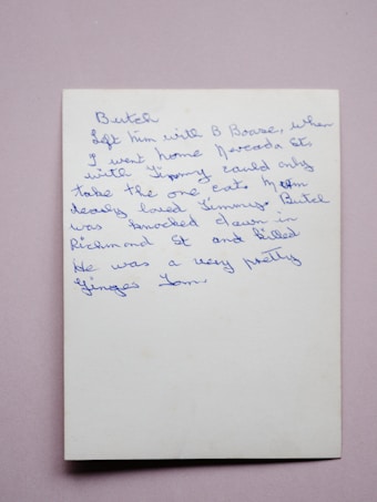 A handwritten note in blue ink on a white piece of paper. The handwriting is cursive and slightly slanted to the right. The background is a plain, soft pink surface.