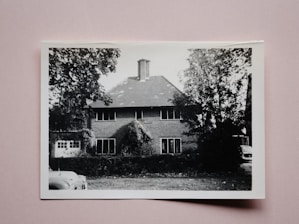 Black and white photo of the house from the early 1900s surrounded by old trees.