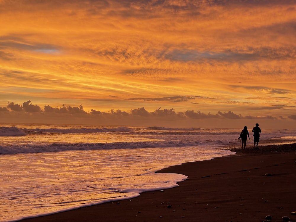 two people standing on a beach watching the sunset