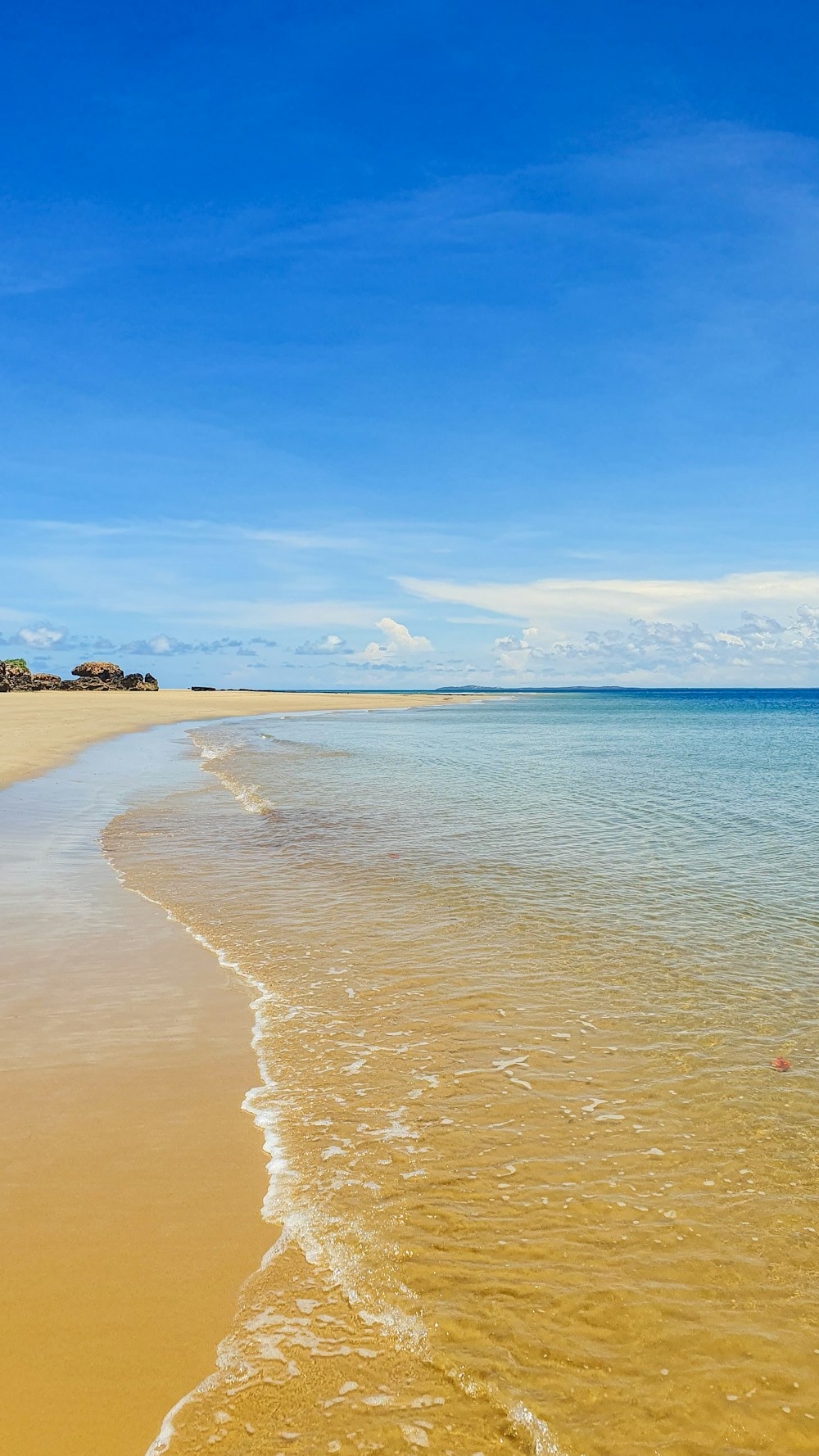 a sandy beach next to the ocean under a blue sky