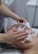 A person is receiving a facial treatment, including the application of a cream or mask. The individual's eyes are closed and a hair cover is worn. A second person is gently applying the treatment with their hands, using a soft cloth to aid the process.