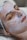 A person is lying down with their eyes closed, seemingly relaxed, while a thick layer of a white facial cream or mask is applied on their face. The head is covered with a protective hairnet, and the person's features indicate they are receiving a beauty treatment.