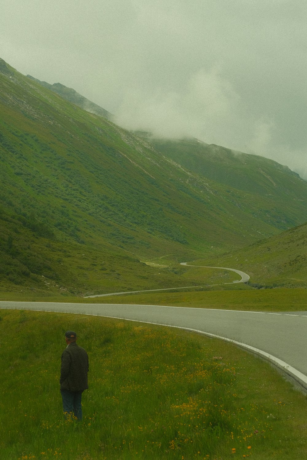a man standing on the side of a road next to a lush green hillside