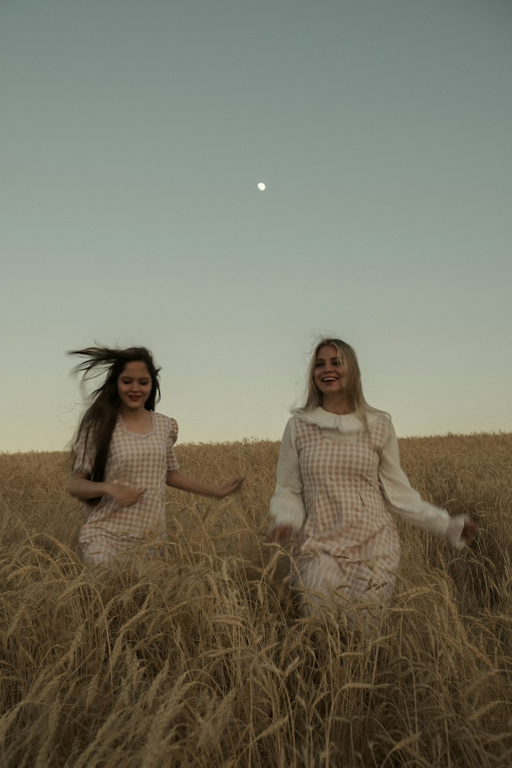 two girls are running through a field of tall grass