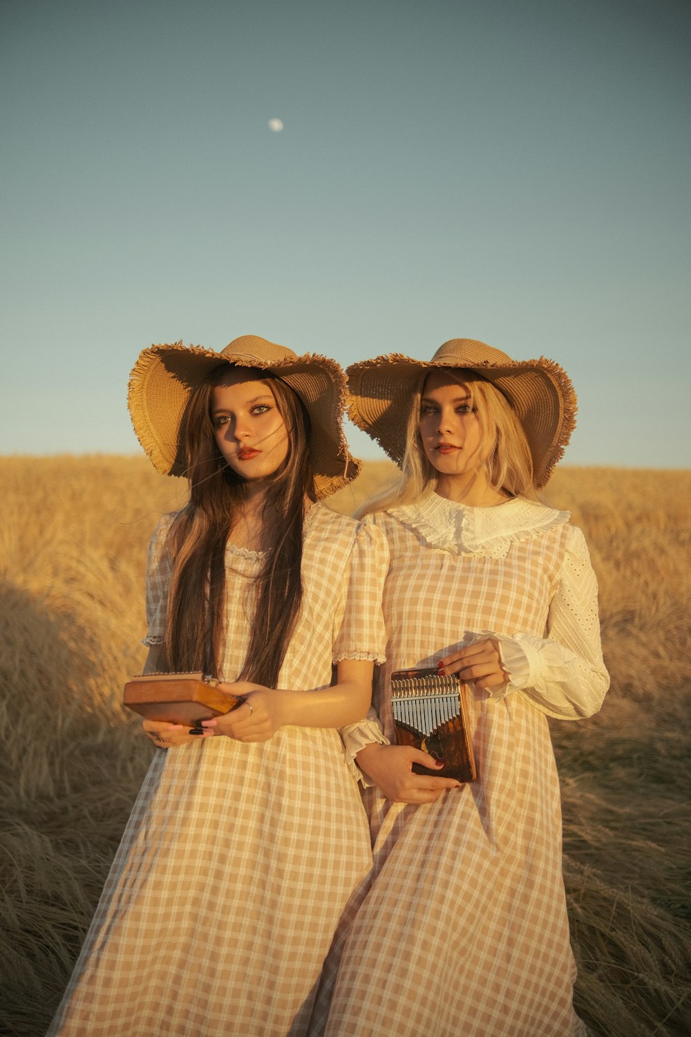 two women in dresses and hats standing in a field