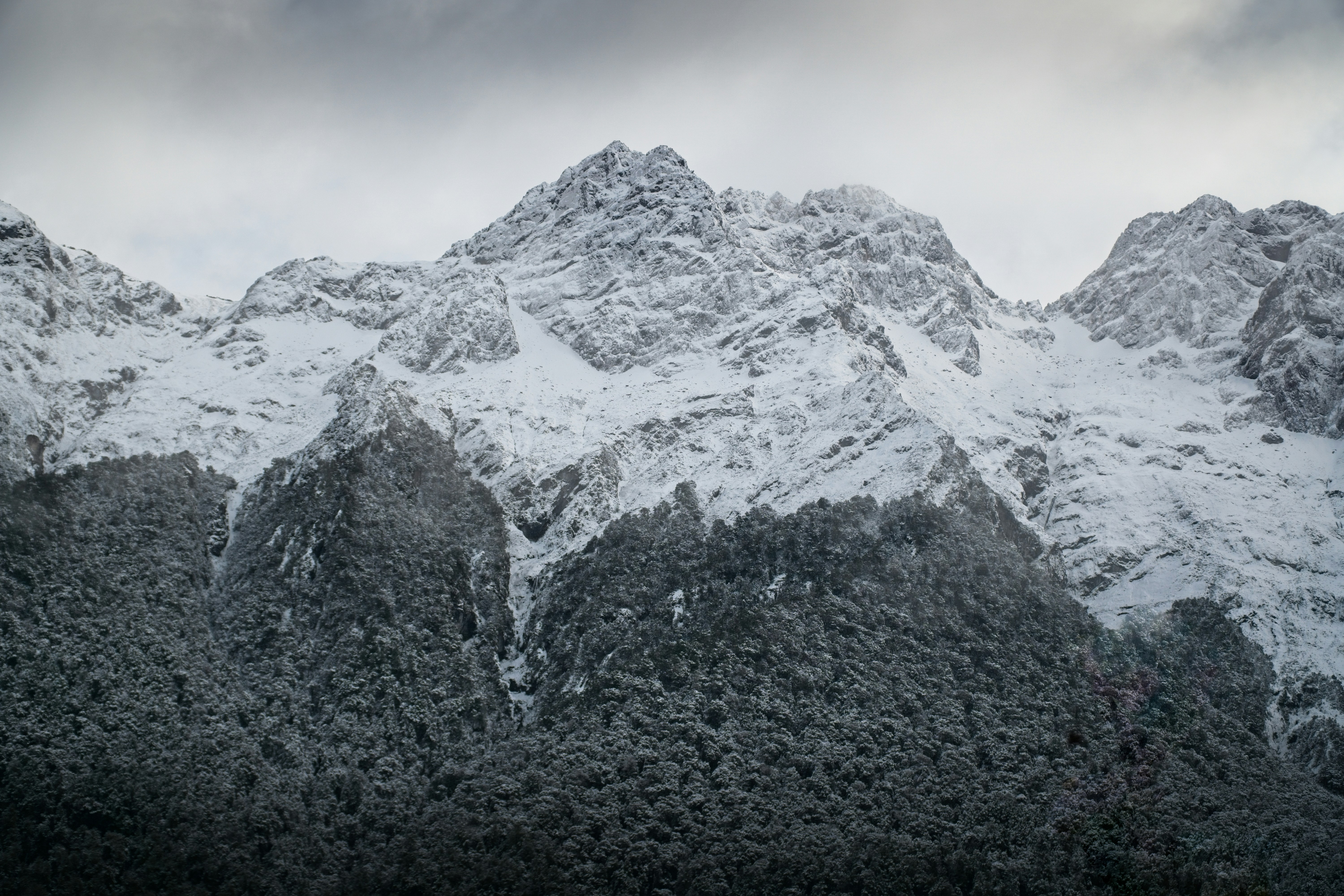 A mountain range covered in snow under a cloudy sky photo – Free ...