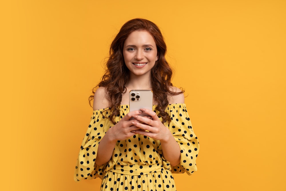 uma mulher em um vestido amarelo de bolinhas segurando um telefone celular