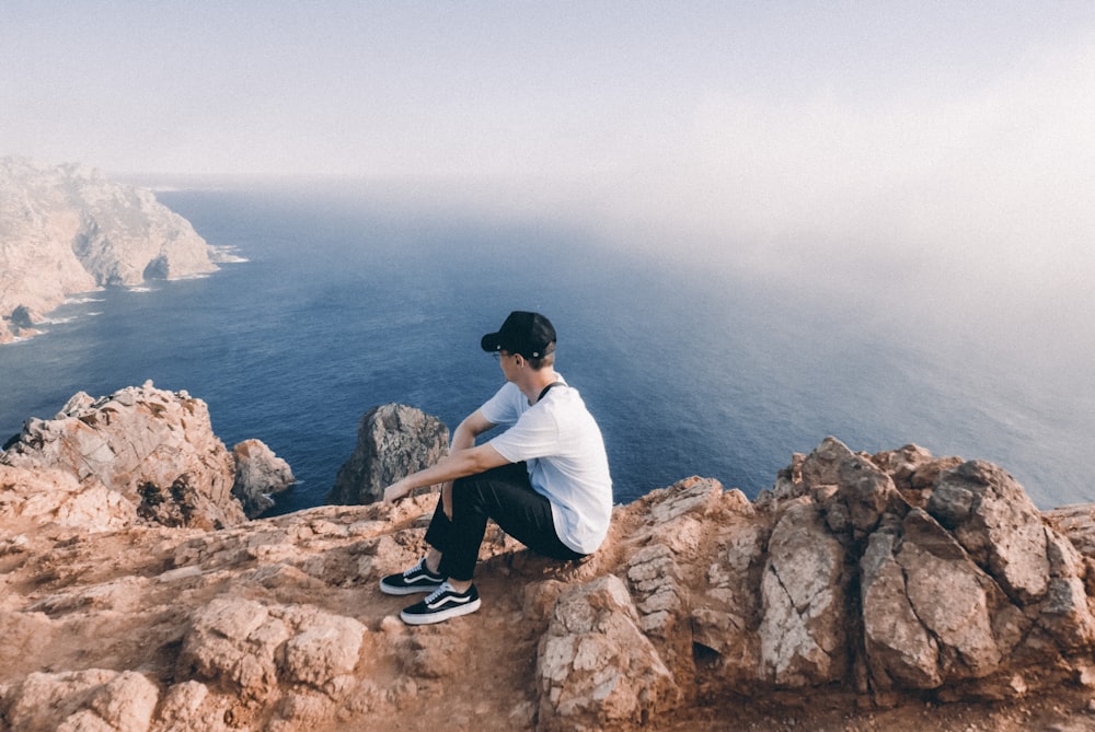 a man sitting on top of a rock next to the ocean