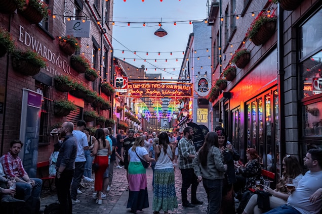 A lively street scene with neon lights and people enjoying drinks outside a bar.