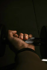 A close-up of a muscular athlete gripping heavy gym weights under moody, dark lighting with neon green accents.