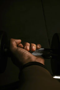 Close-up of hands holding light dumbbells with a soft-focus background of a fitness room.