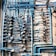 An intricate network of blue pipes and valves is mounted against a tiled wall. Numerous pressure gauges are attached at intervals, providing a detailed and complex arrangement. Each pipe is carefully connected, and there are various fittings and connections visible.