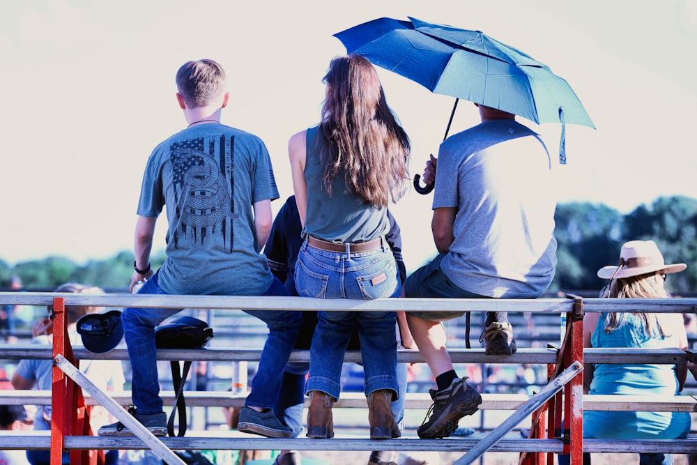 a group of people sitting on a bench under an umbrella