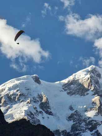 A paraglider soaring gracefully above sunlit mountain ridges under a clear blue sky.