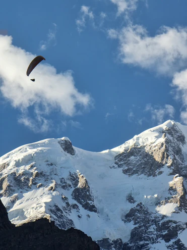 A paraglider soaring gracefully above sunlit mountain ridges under a clear blue sky.
